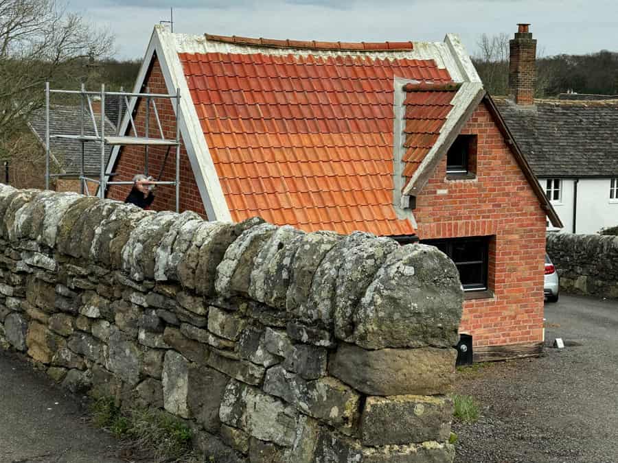 Completed clay-tile re-roof on a brick cottage in Kibworth Harcourt, scaffold still up beside the old stone boundary wall
